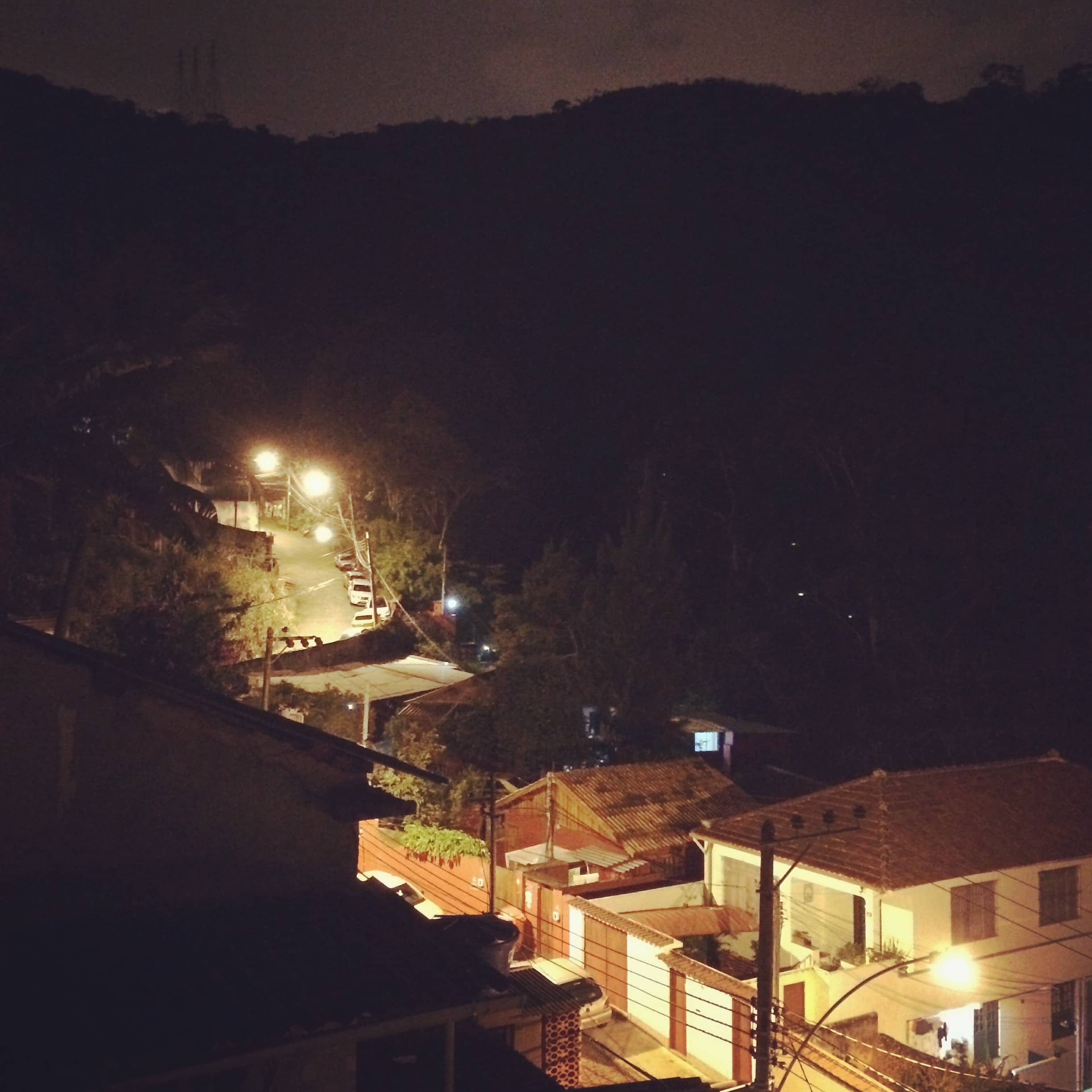 Warm lights illuminate buildings and a road against a dark hillside.