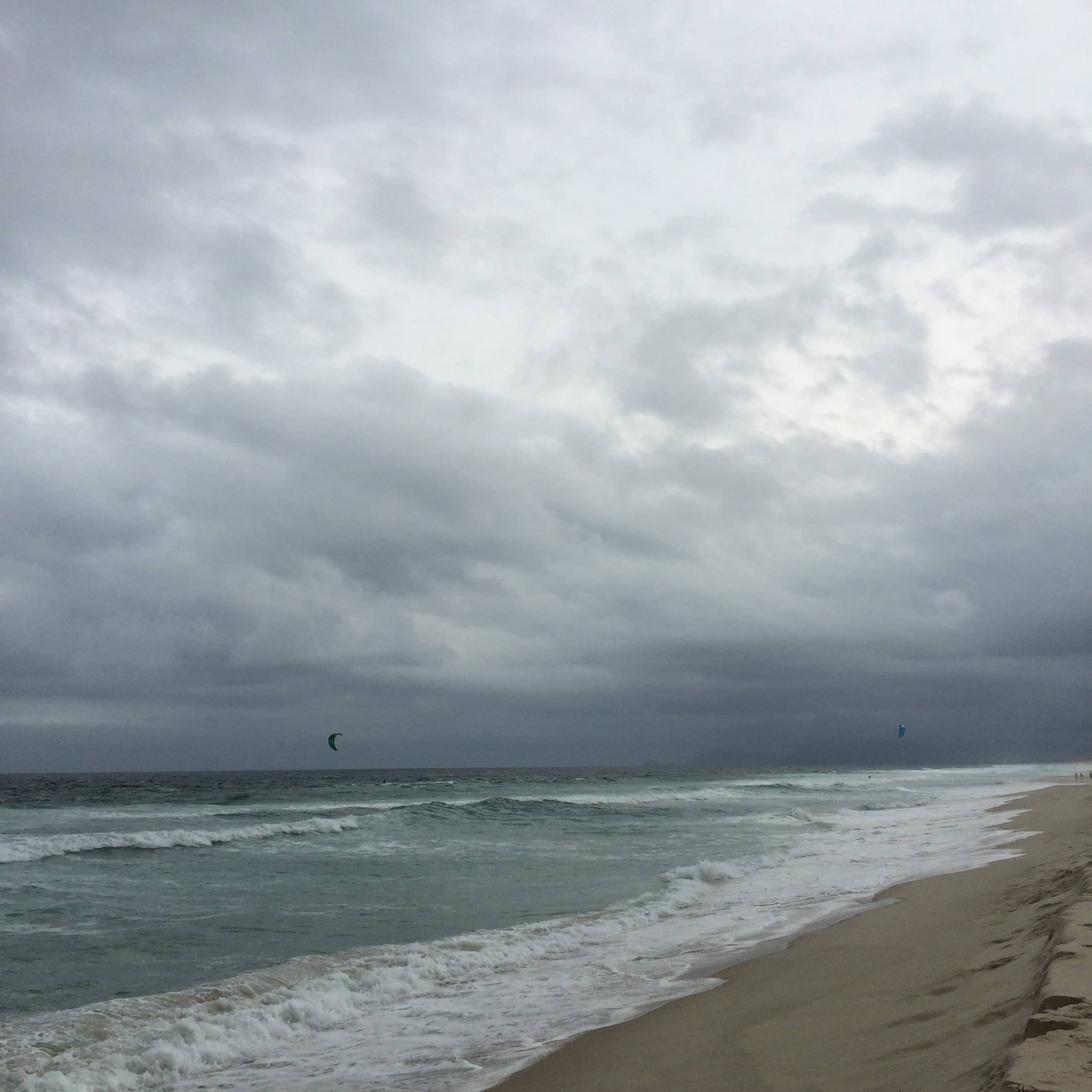 Waves wash onto a sandy beach beneath heavy gray clouds.
