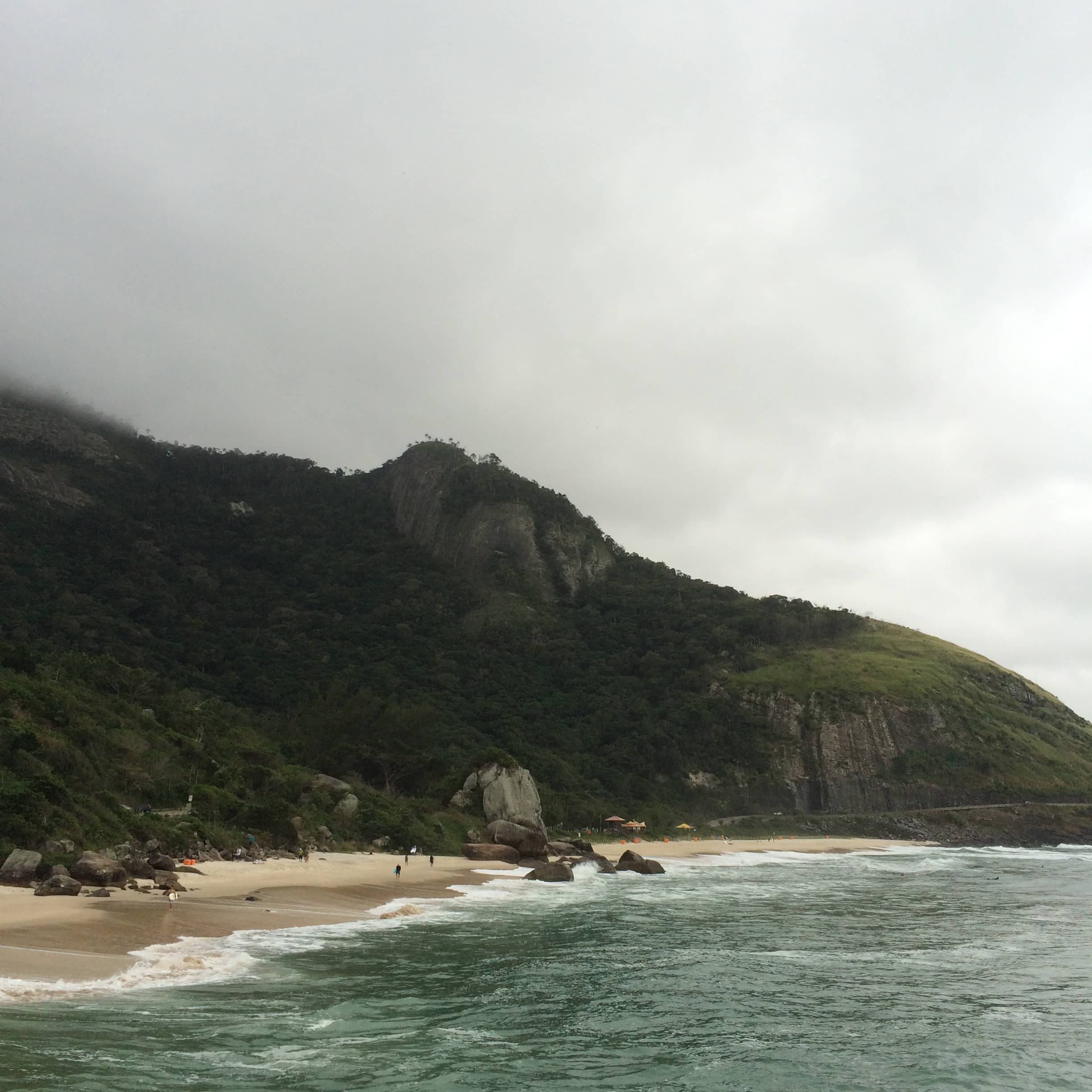 Low clouds cling to a forested mountain beside a sandy shoreline.