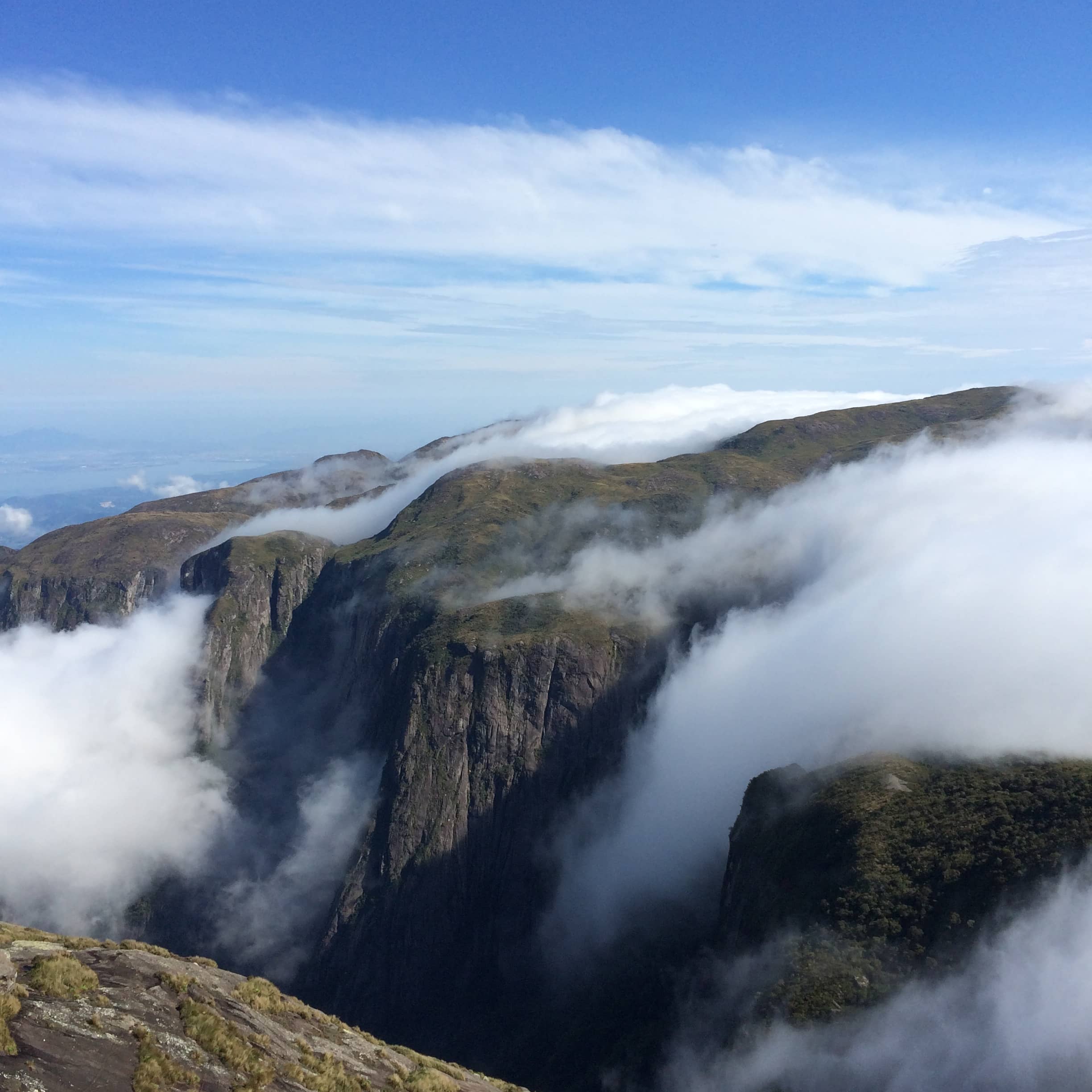 Clouds drift between steep mountain cliffs beneath a blue sky.