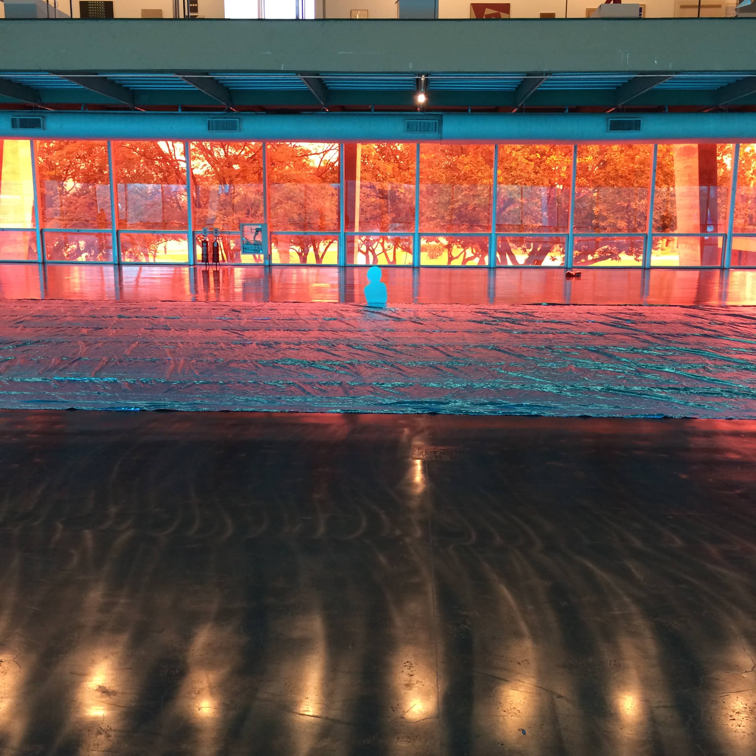 Orange and red light shines through a glass-walled interior onto a reflective floor.