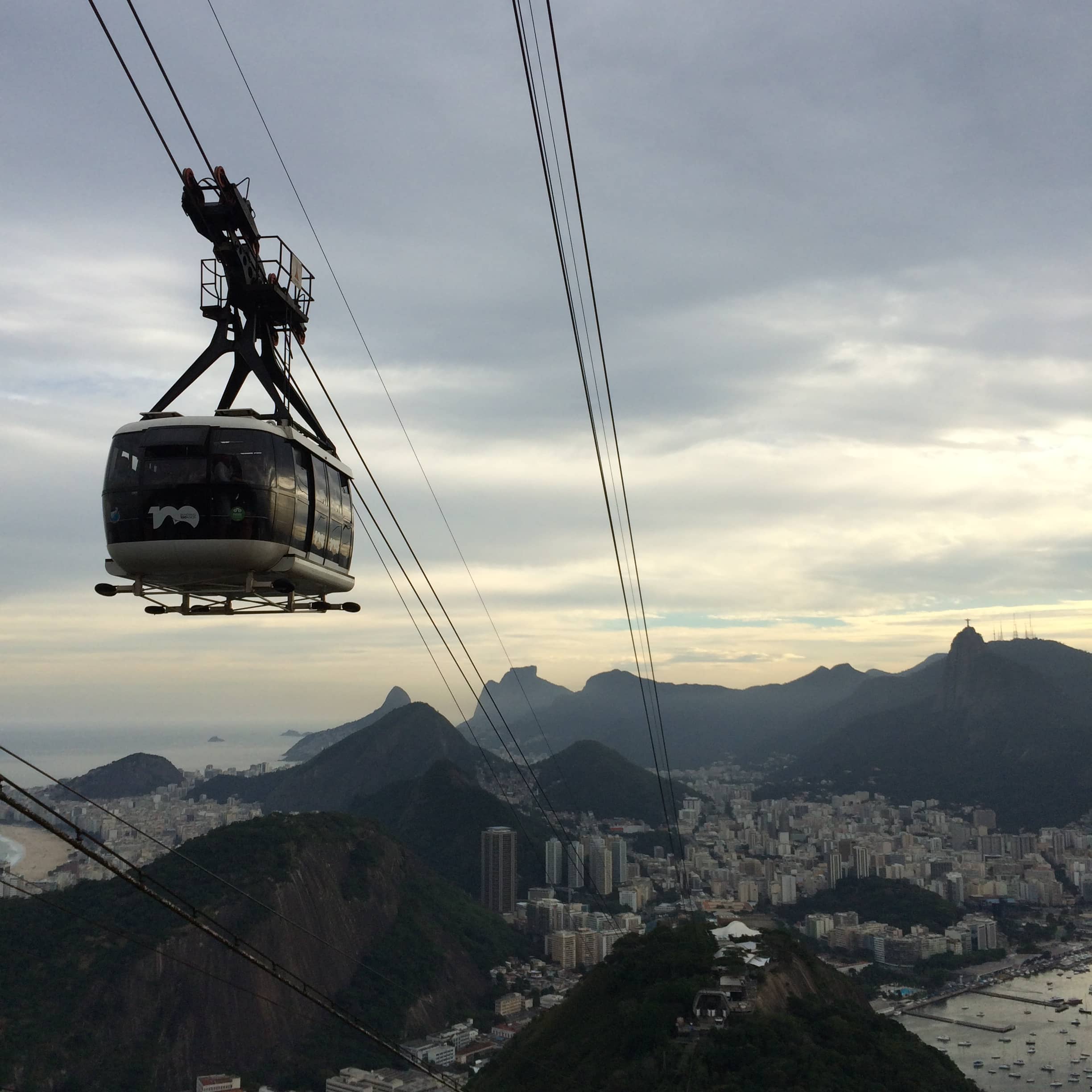 A cable car hangs above the city with mountain silhouettes in the distance.