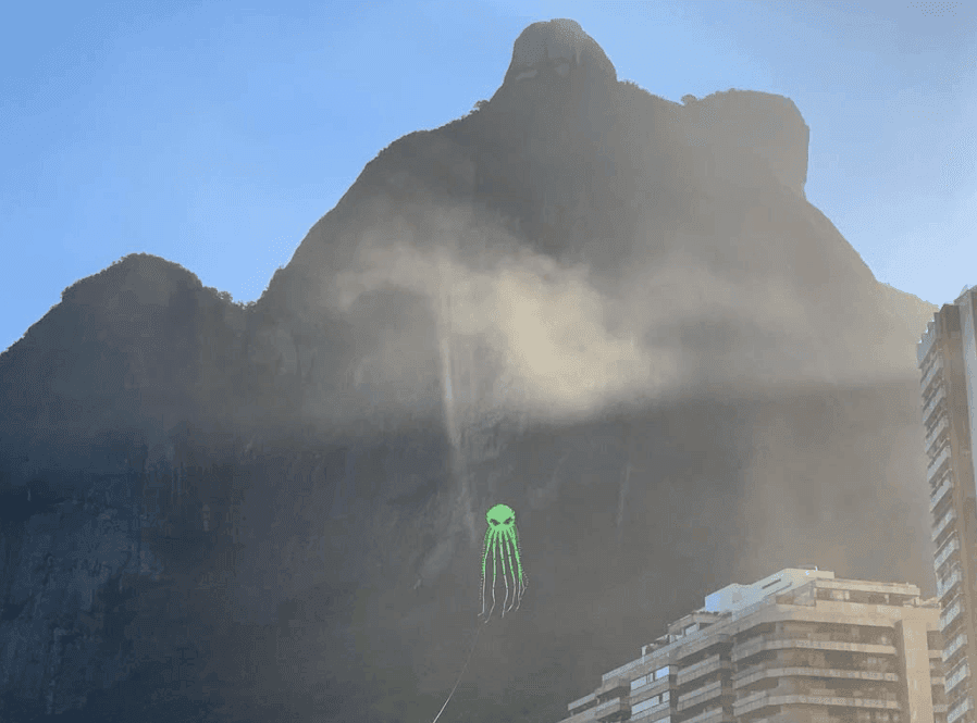 Sunlight and mist soften the outline of a steep mountain above nearby buildings.