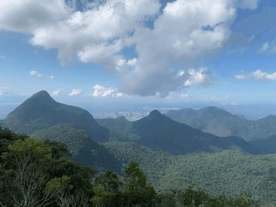 Layers of forested mountains stretch beneath scattered white clouds.