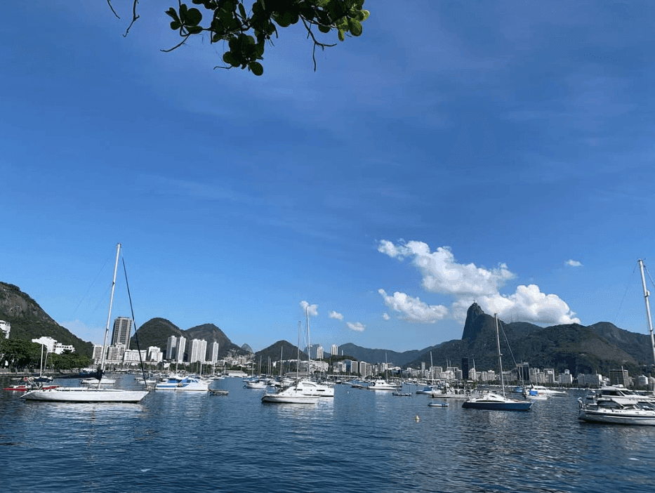 Sailboats and yachts sit on calm water with buildings and mountains beyond.