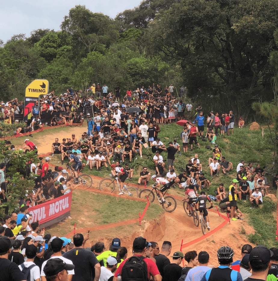 Spectators gather around a winding dirt cycling course on a grassy hillside.