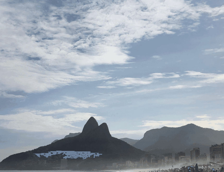 Two pointed mountain peaks rise above a hazy city under a textured sky.