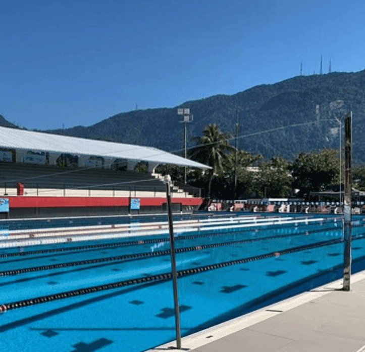 An outdoor lap pool stretches beneath a forested mountain and a clear blue sky.