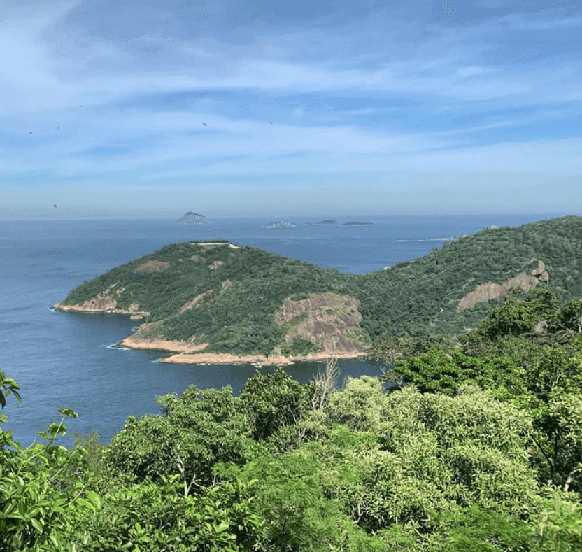 Lush green hills frame a sheltered bay and the open ocean beneath a lightly clouded sky.