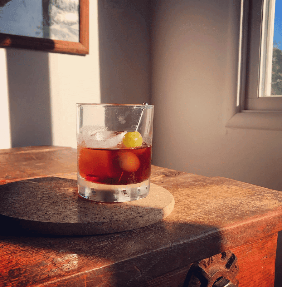 An amber drink with citrus rests on a wooden table in warm window light.