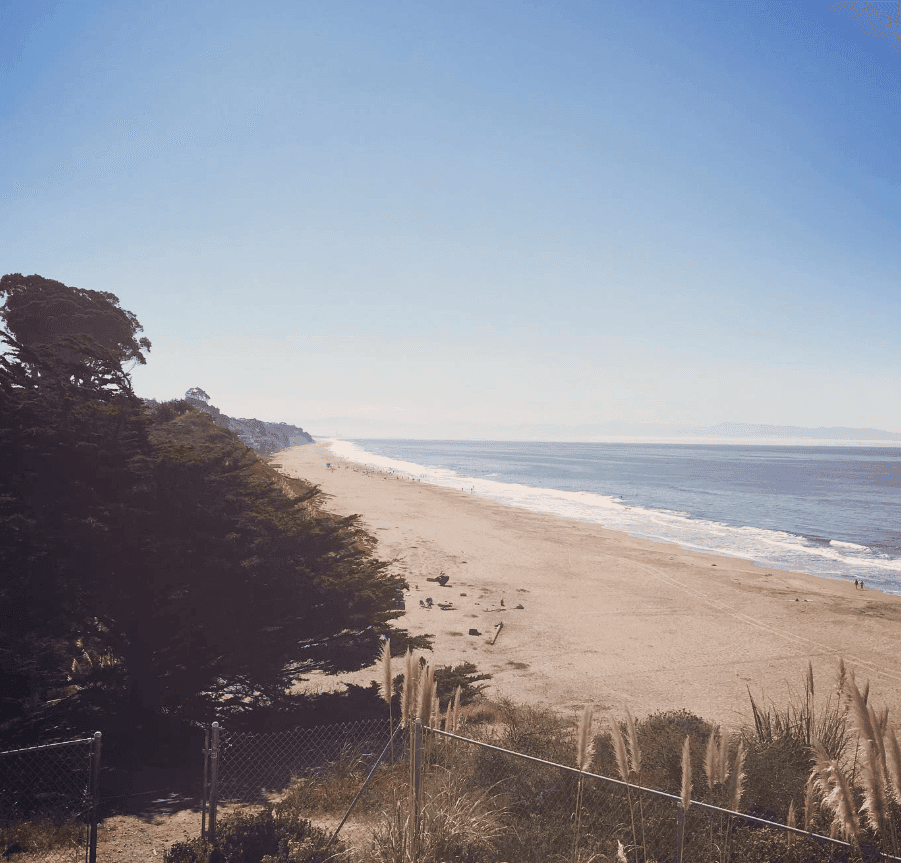 A broad sandy beach curves along the ocean beneath a clear blue sky.