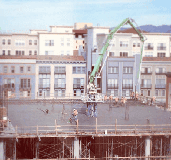 Construction equipment and scaffolding stand in front of a row of city buildings.