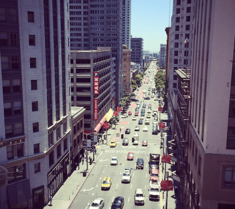 An elevated view looks down a busy avenue between tall city buildings.