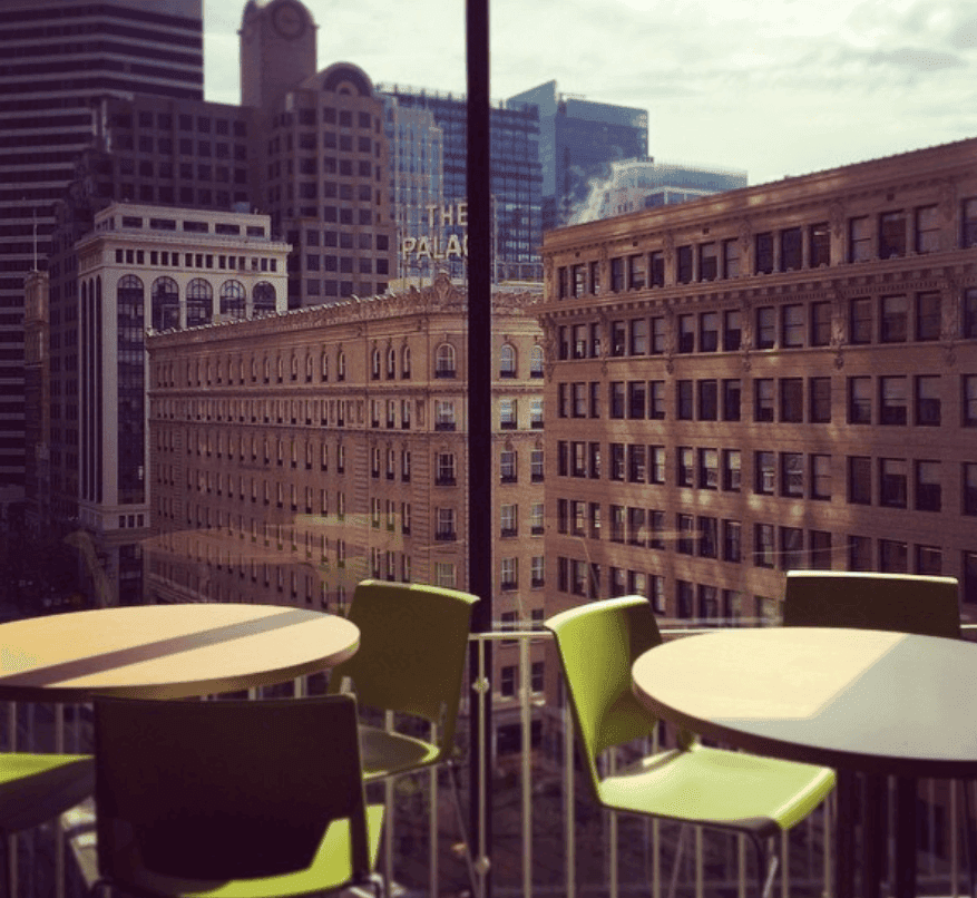 Bright green chairs and round tables overlook downtown buildings from a terrace.