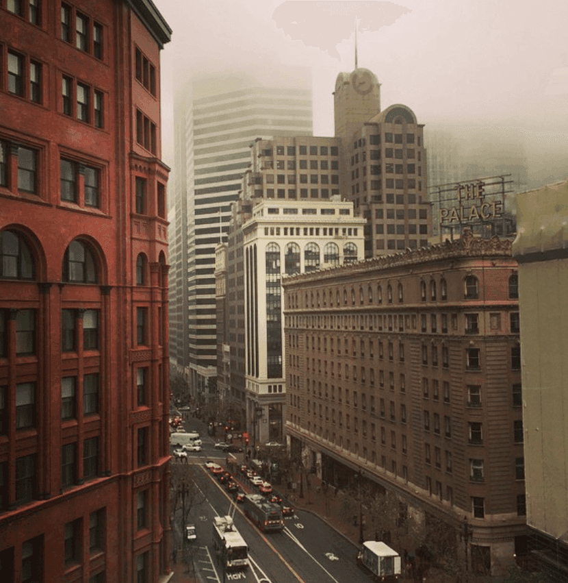 Historic and modern buildings line a city street beneath low fog.