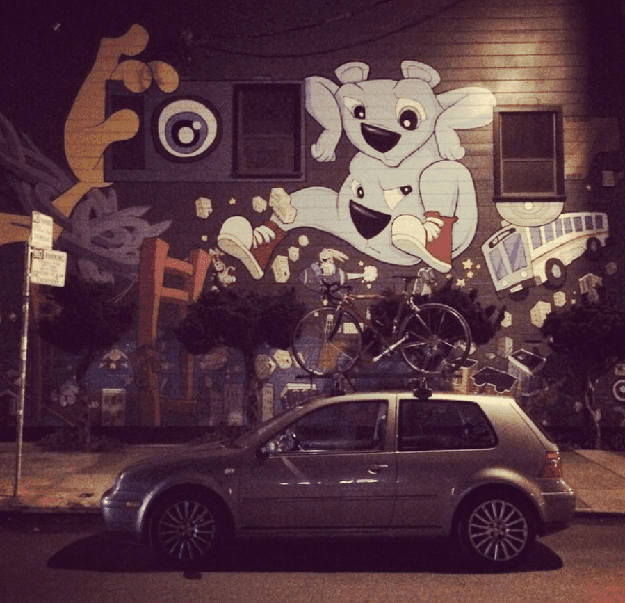 A large playful mural overlooks a parked car on a city street at night.