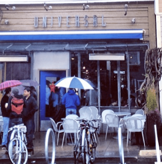 People and parked bicycles gather outside a cafe with sidewalk tables.