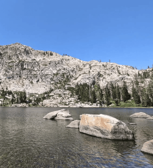 Large boulders sit in a mountain lake beneath a steep granite ridge.