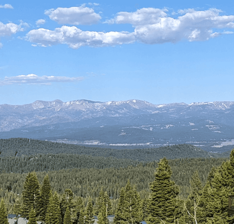 Pine-covered slopes open onto a broad valley and distant mountain ranges.