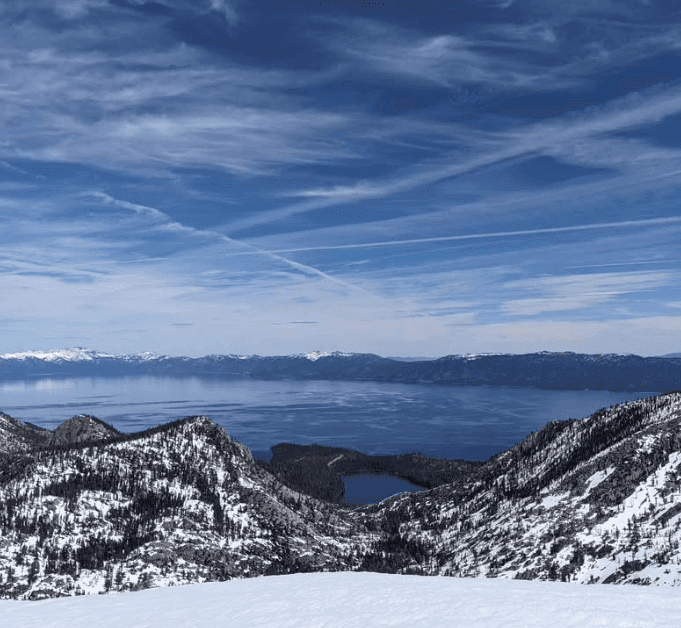 A blue lake appears beyond snow-covered ridges under streaked clouds.