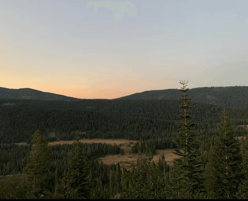 A warm sunset glow rests above dark wooded hills.