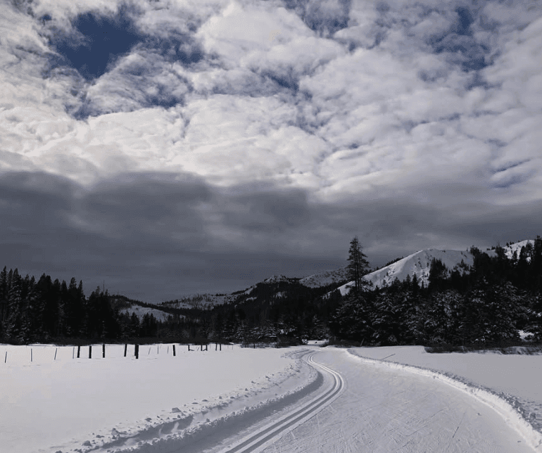 Parallel tracks curve through a snowy landscape beneath textured clouds.