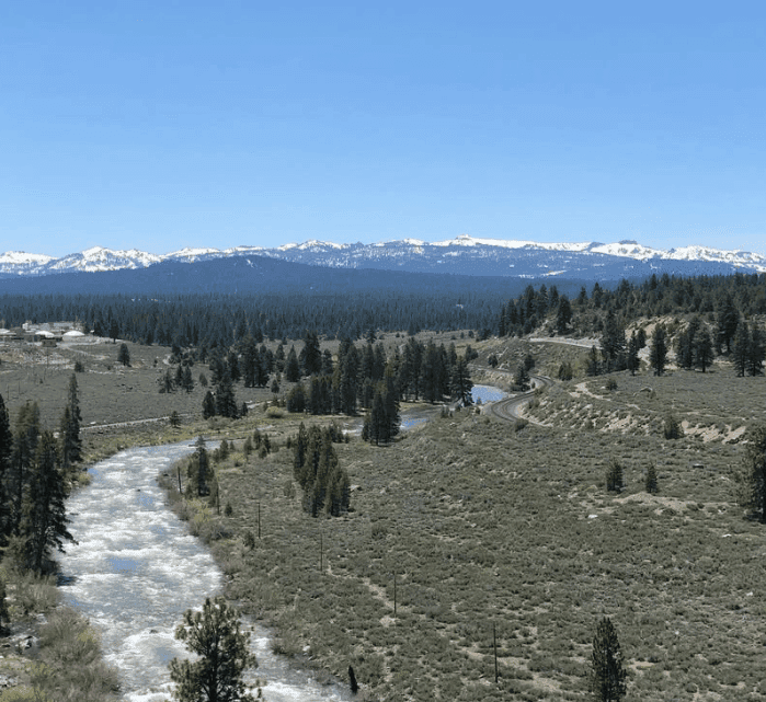 A winding creek crosses an open meadow with snowy mountains on the horizon.