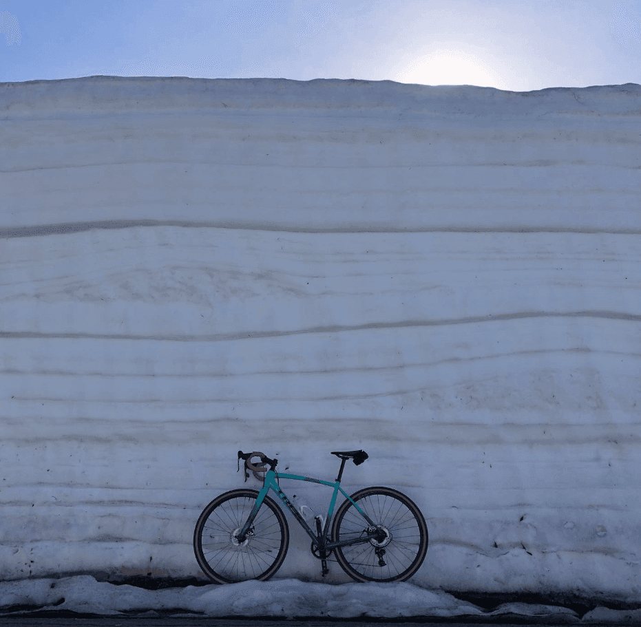 A bicycle leans against a towering wall of plowed snow.