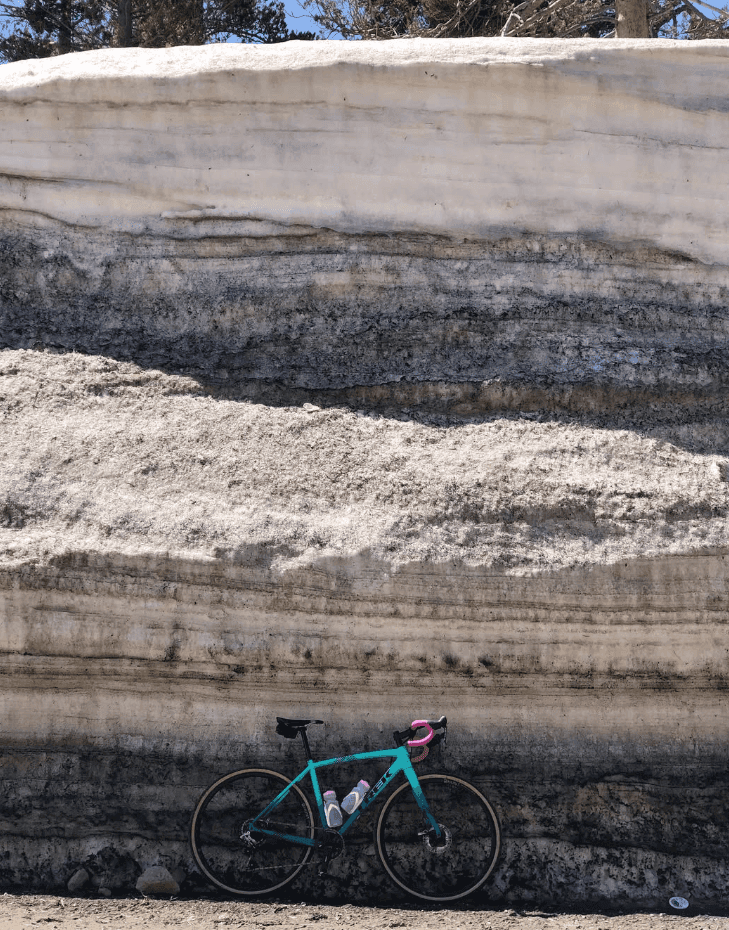A bicycle rests against a high snowbank marked by dark horizontal layers.